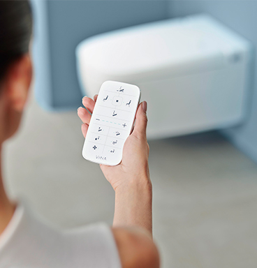 Woman holding remote control in front of VitrA V-Care shower toilet